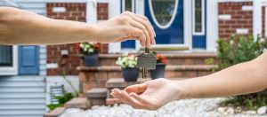 Arm of man placing house keys in the hand of a woman in front of a home.