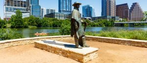 Stevie Ray Vaughan statue with Austin skyline and kayaker in the background.