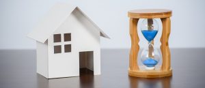 White miniature home next to an hourglass with blue sand.